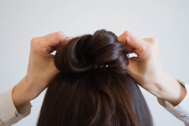 A woman with brown hair ties her hair into a bun